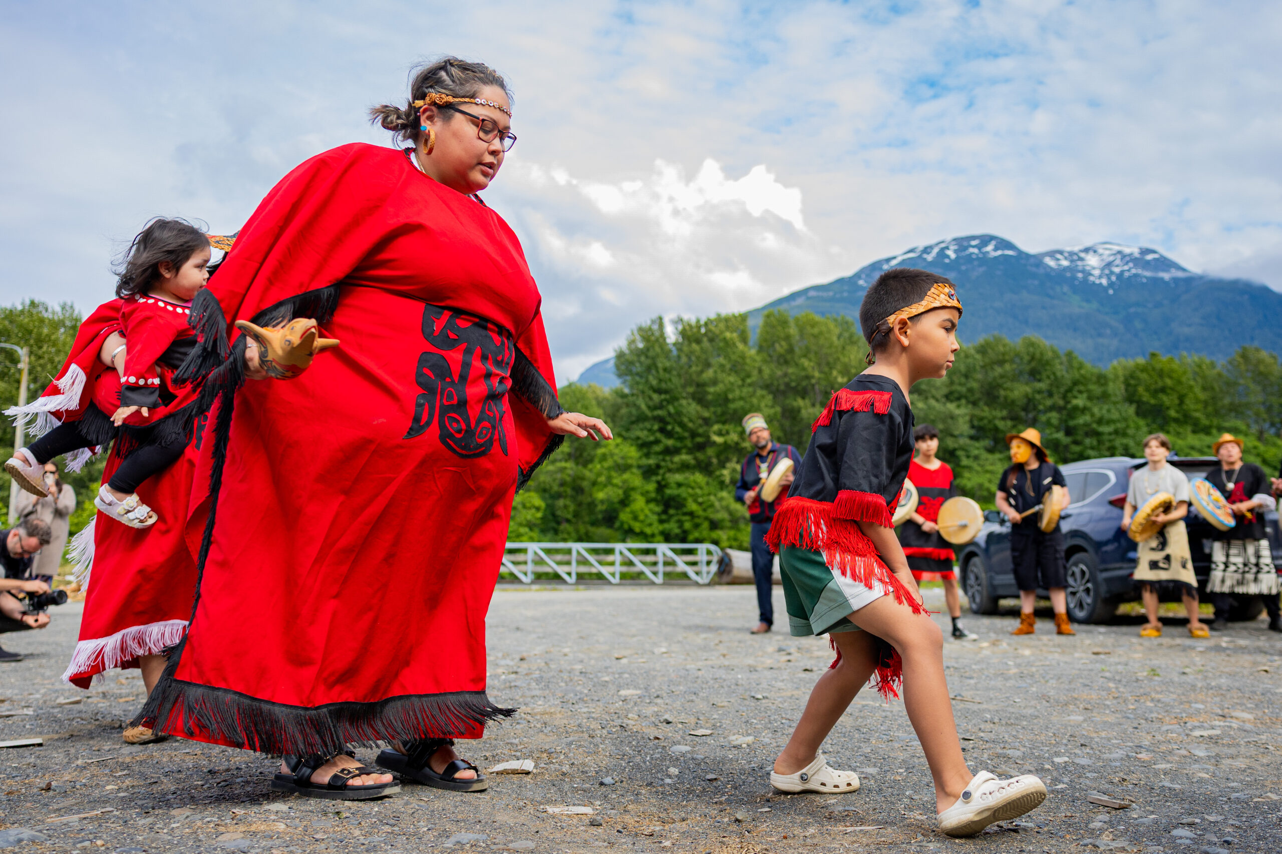A woman and child, both wearing red, traditional clothing, dance outdoors.